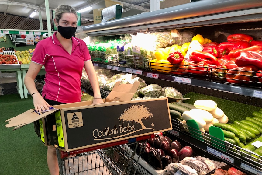 Woman restocks supermarket shelves with vegetables