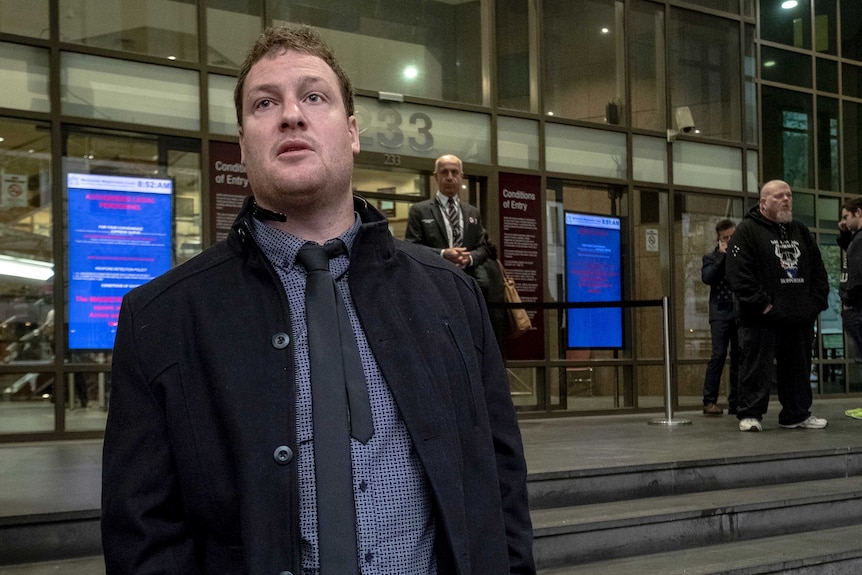 Ricky Turner, dressed in a blue shirt and black tie and jacket, stands outside Melbourne Magistrates' Court.