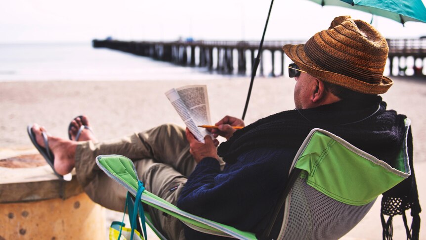 A man with a book in a camp chair on the beach 