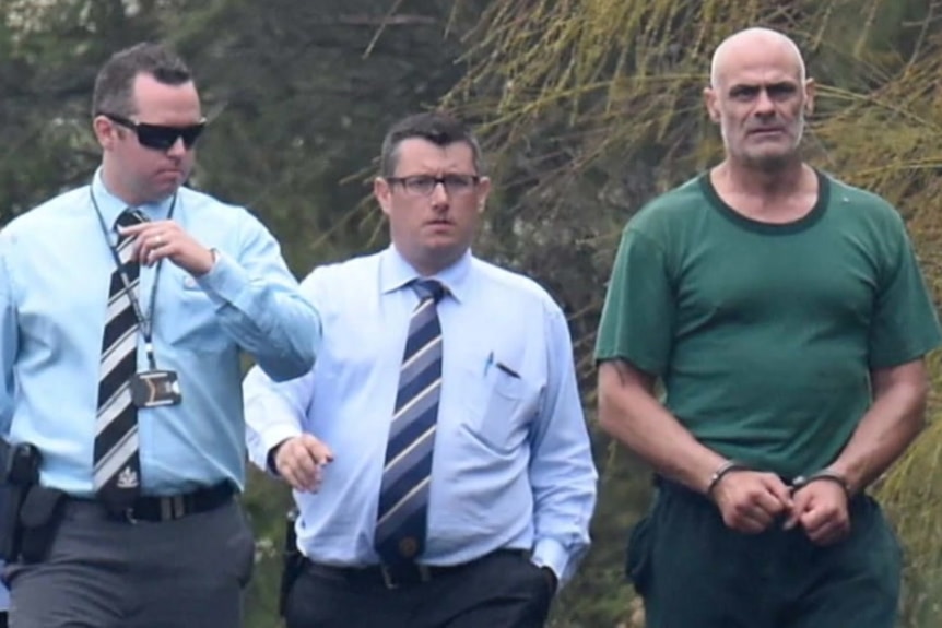 Vinzent Tarantino in handcuffs walking with police in bushland