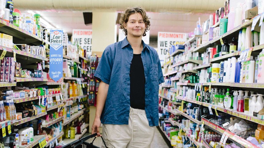 Young man Mitch stands in the middle of the supermarket aisle with a basket