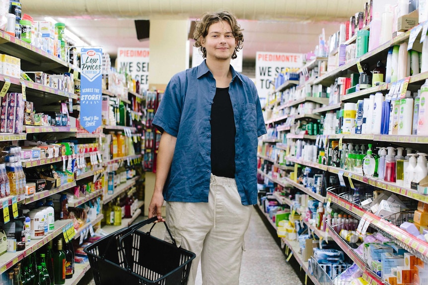 Young man Mitch stands in the middle of the supermarket aisle with a basket