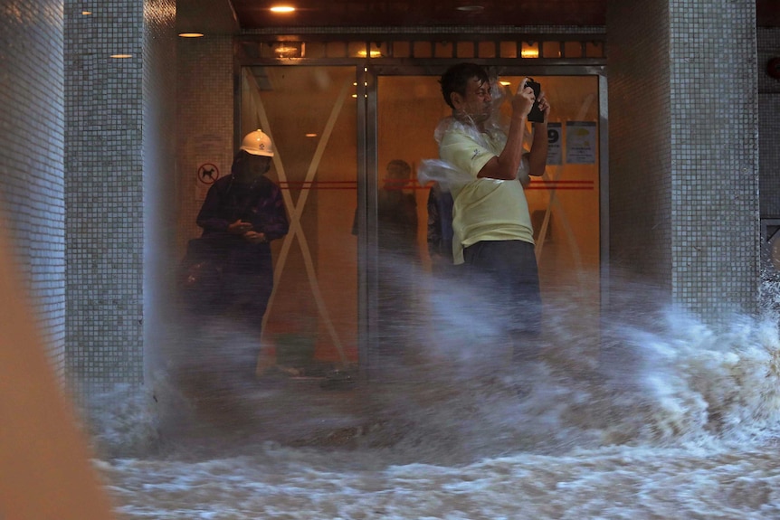 A man attempts to take a picture while being blown by strong winds and flood water in Hong Kong