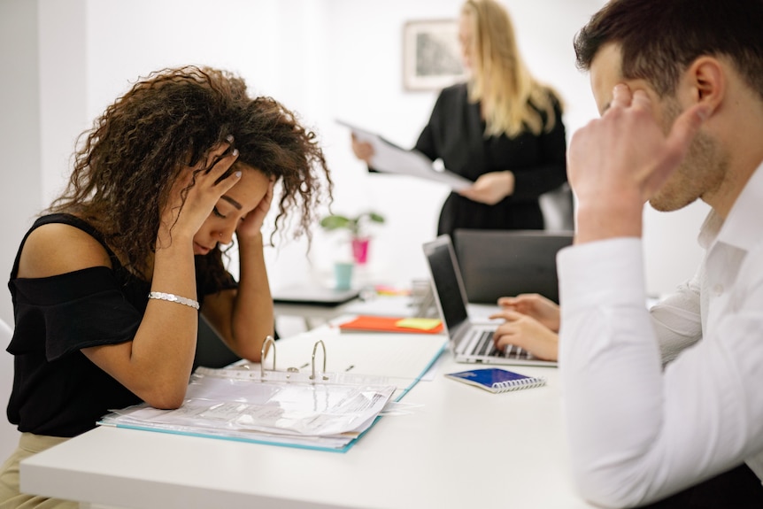 A woman looks stressed while looking at paperwork in an office.