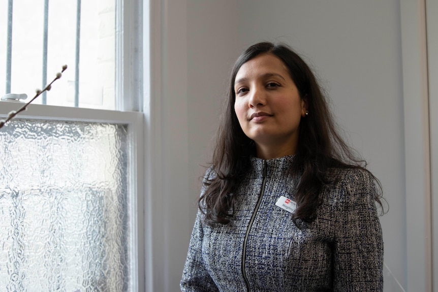 A woman in business attire and wearing a nametag stands in front of a window.