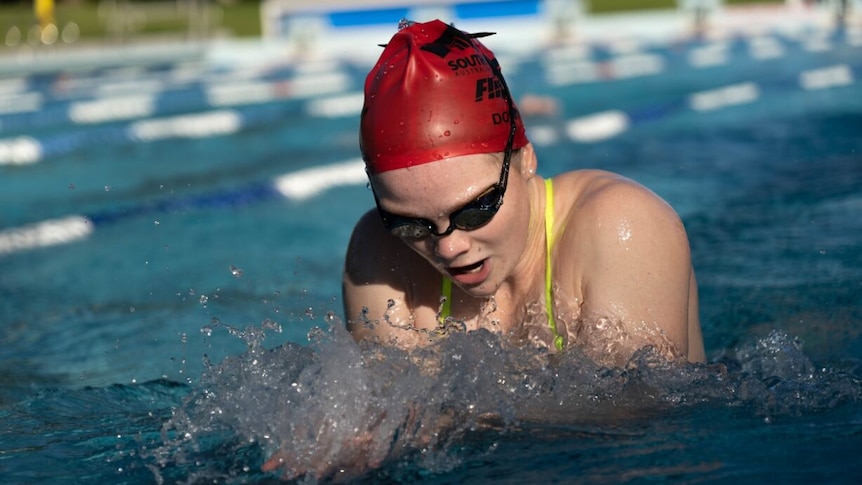 Girl wearing colourful bathers and red swimming cap mid-freestyle stroke in a pool.