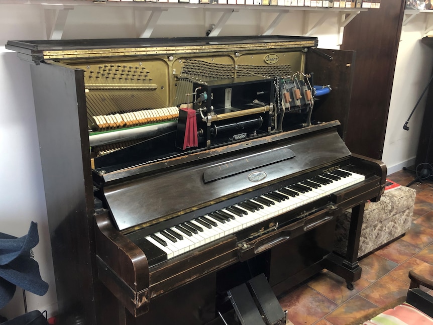 An old wooden pianola with the front taken off, showing the workings