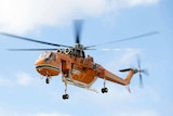 An orange helicopter hovers in mid-air.