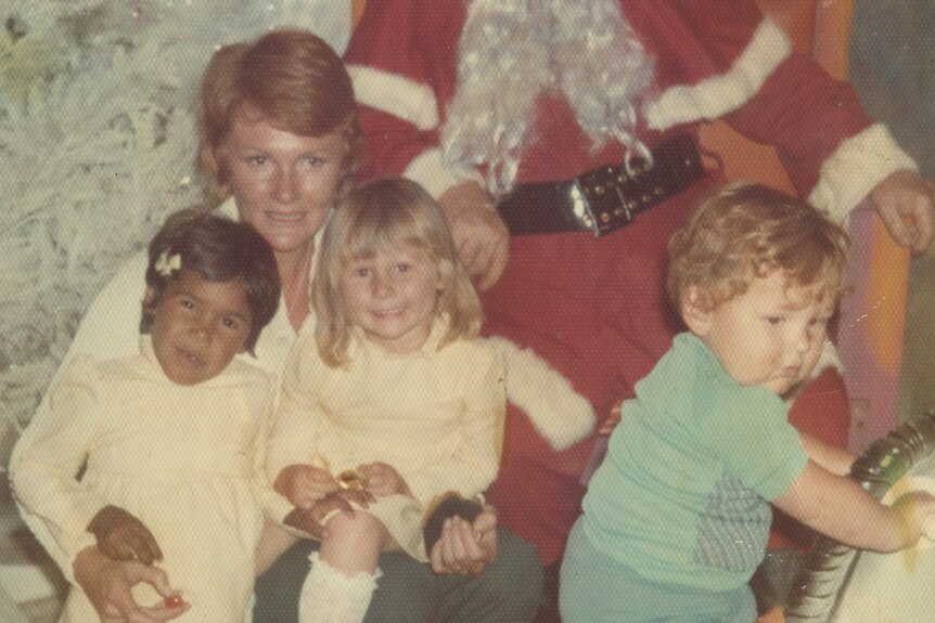 An old photo of a little black and white girl sitting on a lady's knee in front of a person dressed as santa