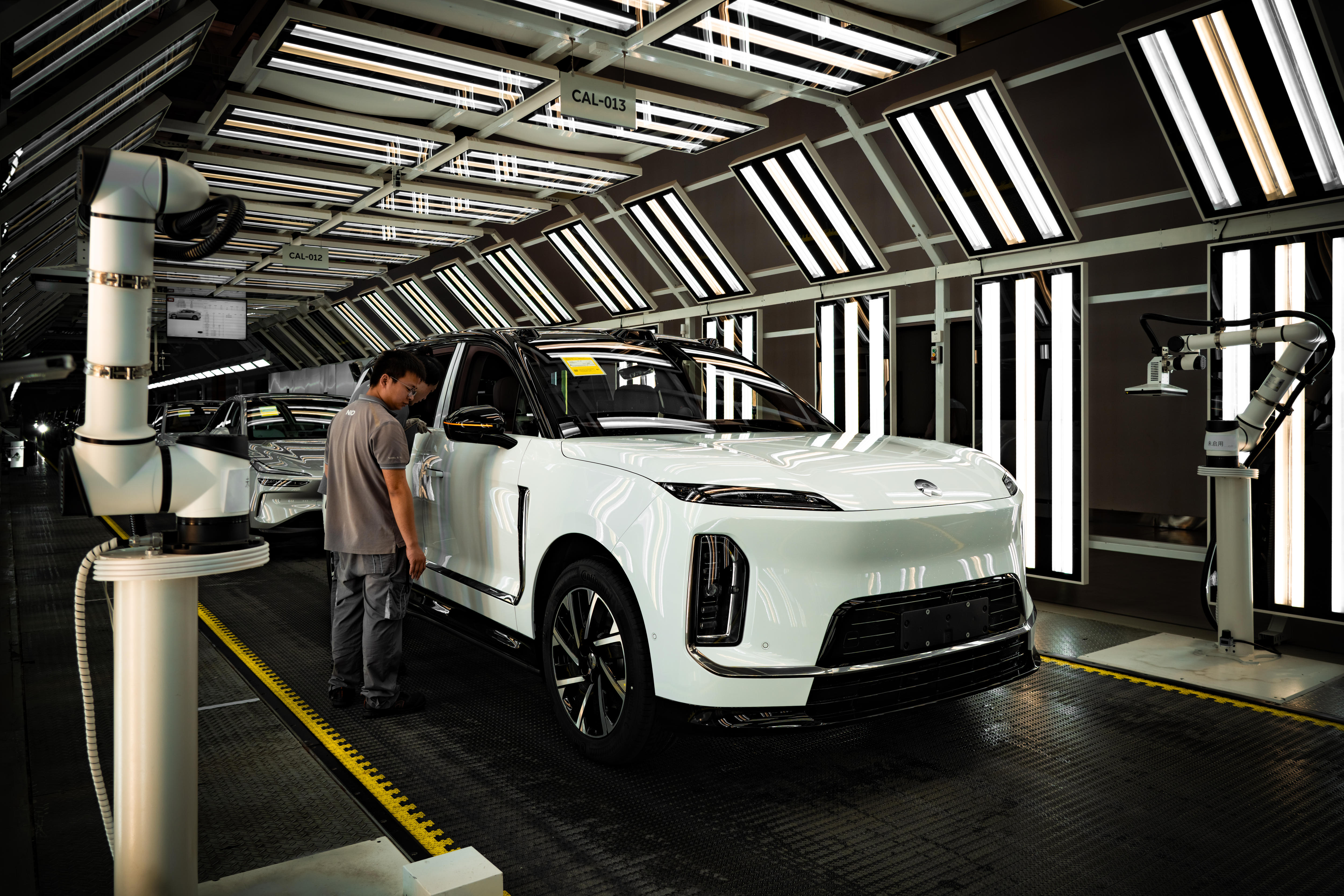 A white electric vehicle inside a factory, with a man standing beside it.