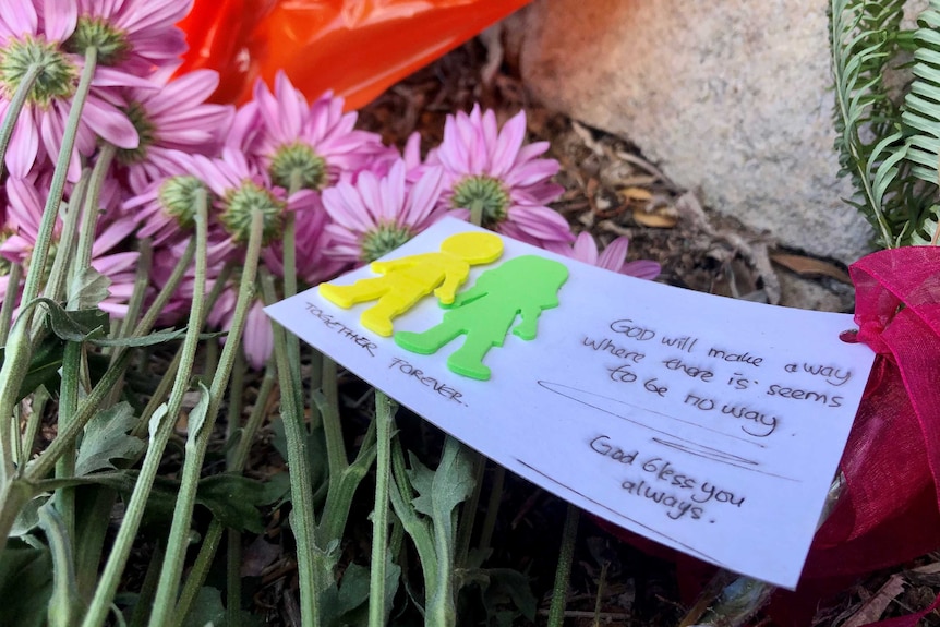 Written tribute and flowers on the driveway of the house where the bodies of Loris and Franco Puglia were found inside the home.