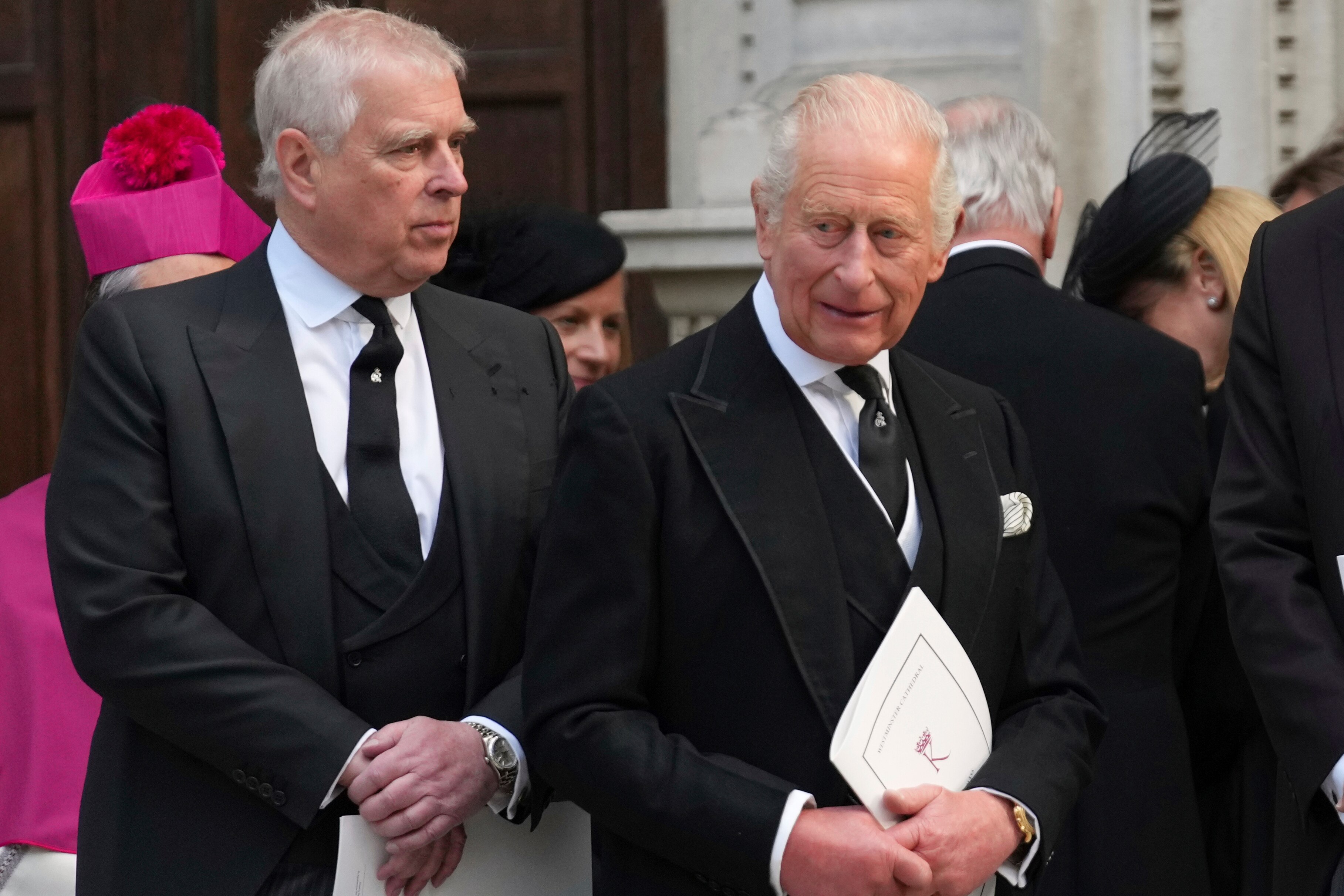 King Charles and Andrew Mountbatten Windsor in black suits and ties, as the King holds a paper booklet