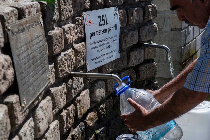 A man collects from a natural spring outlet with a sign that reads "25L per person per fill".