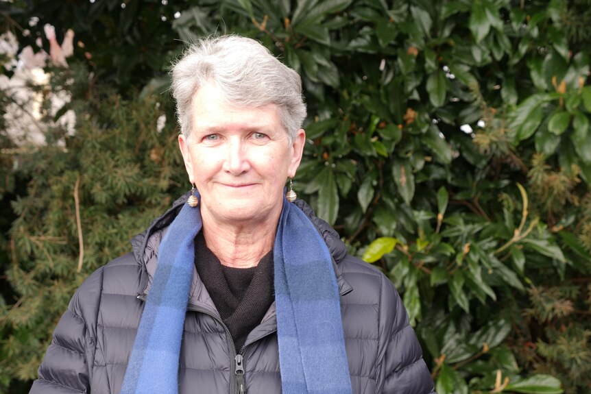 A middle aged lady with a scarf in front of some bushes 