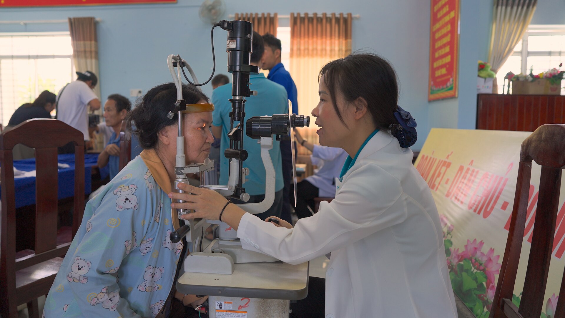 mid shot of an elderly asian woman looking into an eye examination machine (left), a young asian female doctor examining