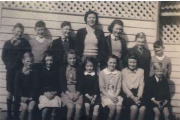 A dozen students and teacher pose in 1940s black and white school photo. 