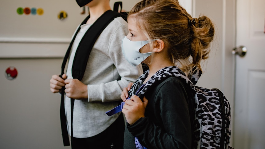 Two children weariing a mask and carrying backpacks