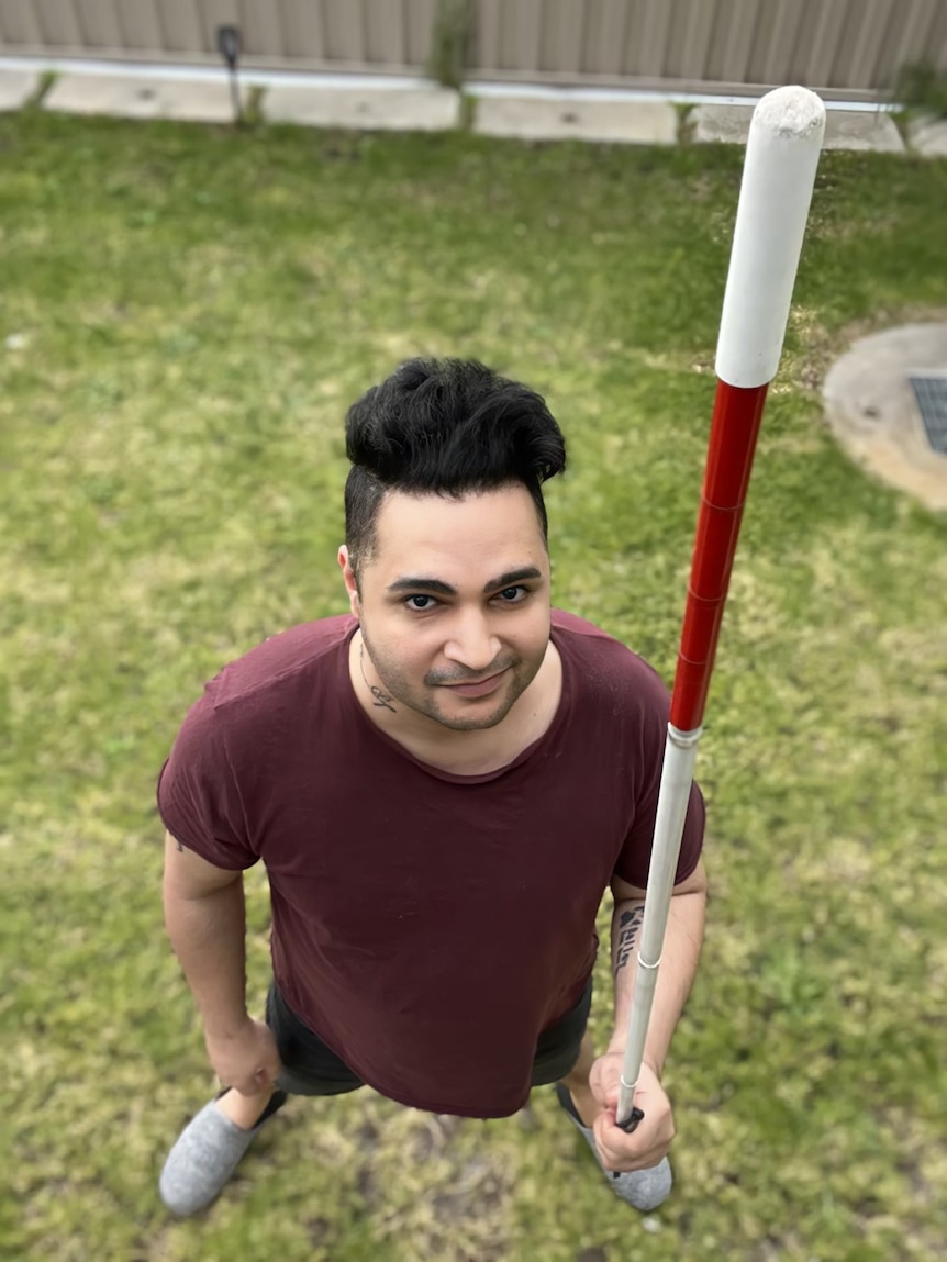 High angle of man looking up at the camera, holding his white cane pointing up to the sky.