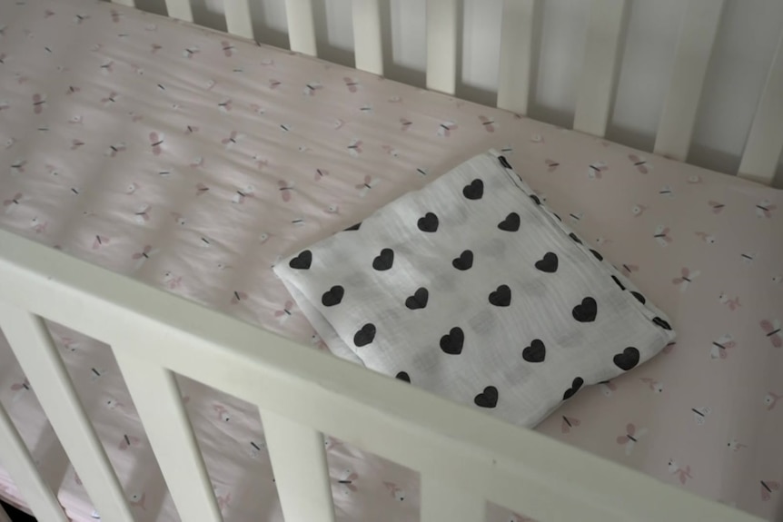A folded blanket with black hearts sits in an empty cot.
