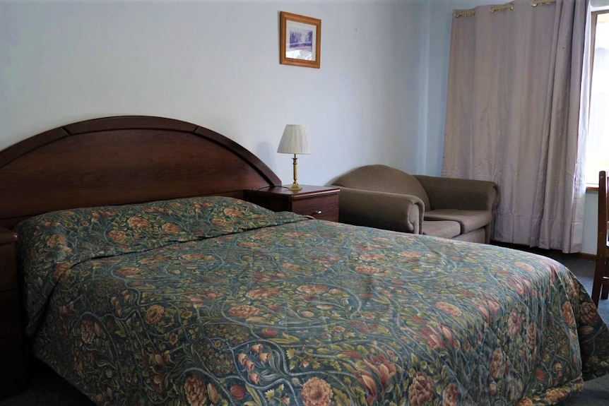 Double bed with a dark wooden headboard and matching bedside tables. There are lamps on either one and a small couch next to it