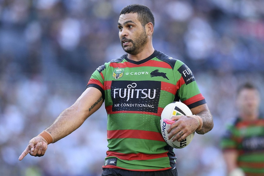 Greg Inglis points at the ground with the ball under his other arm