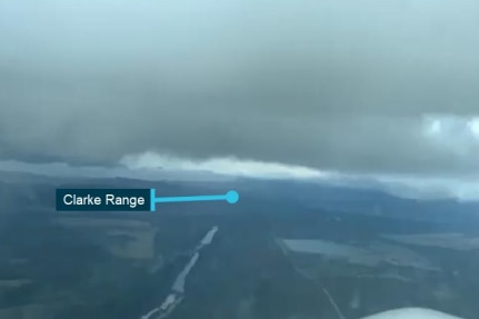 The view out of the front of a light plane, showing cloudy skies and a text marker for the Clarke Range.