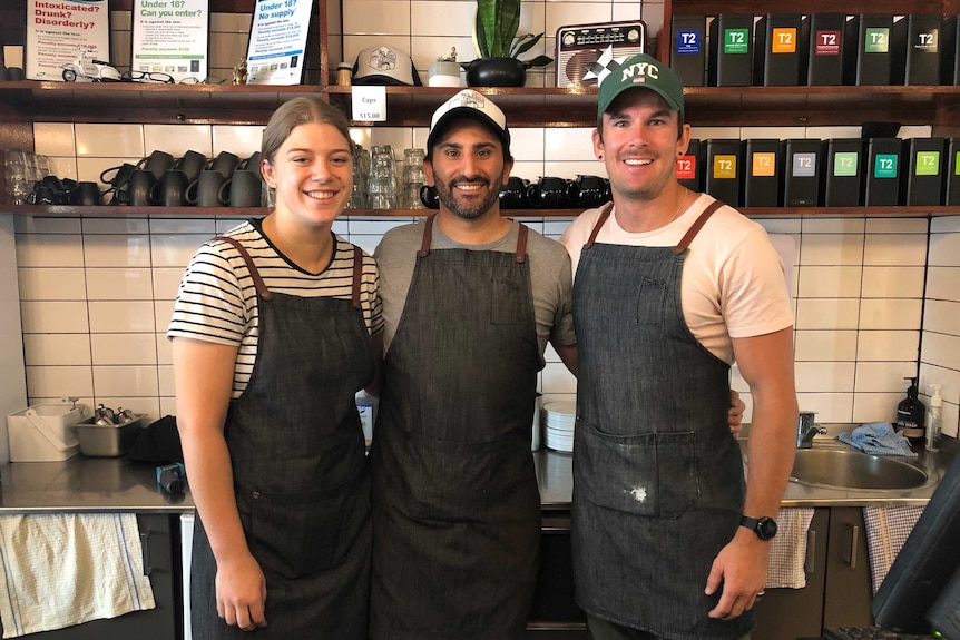 Three cafe staff smile in front of shelves with cups and canisters of tea