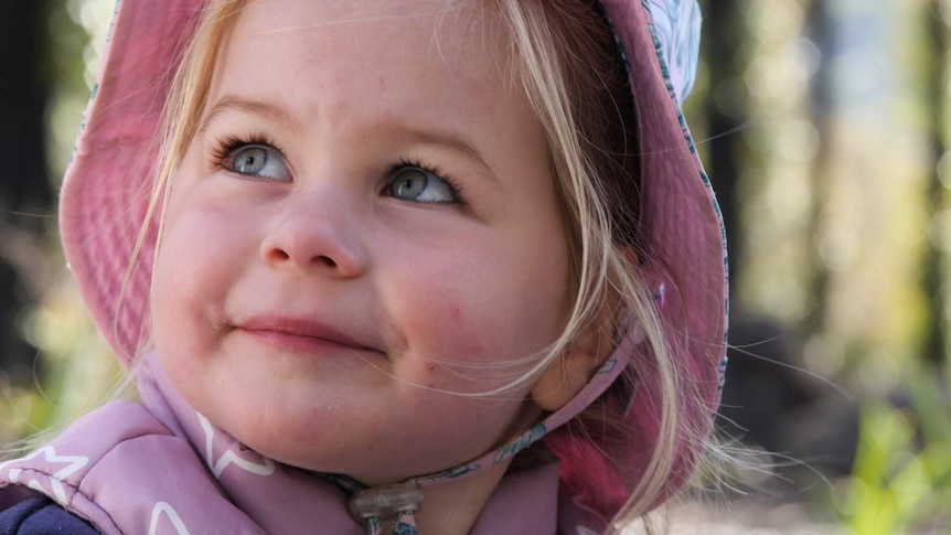 Preschool-age girl in burnt forest looking up off camera smiling