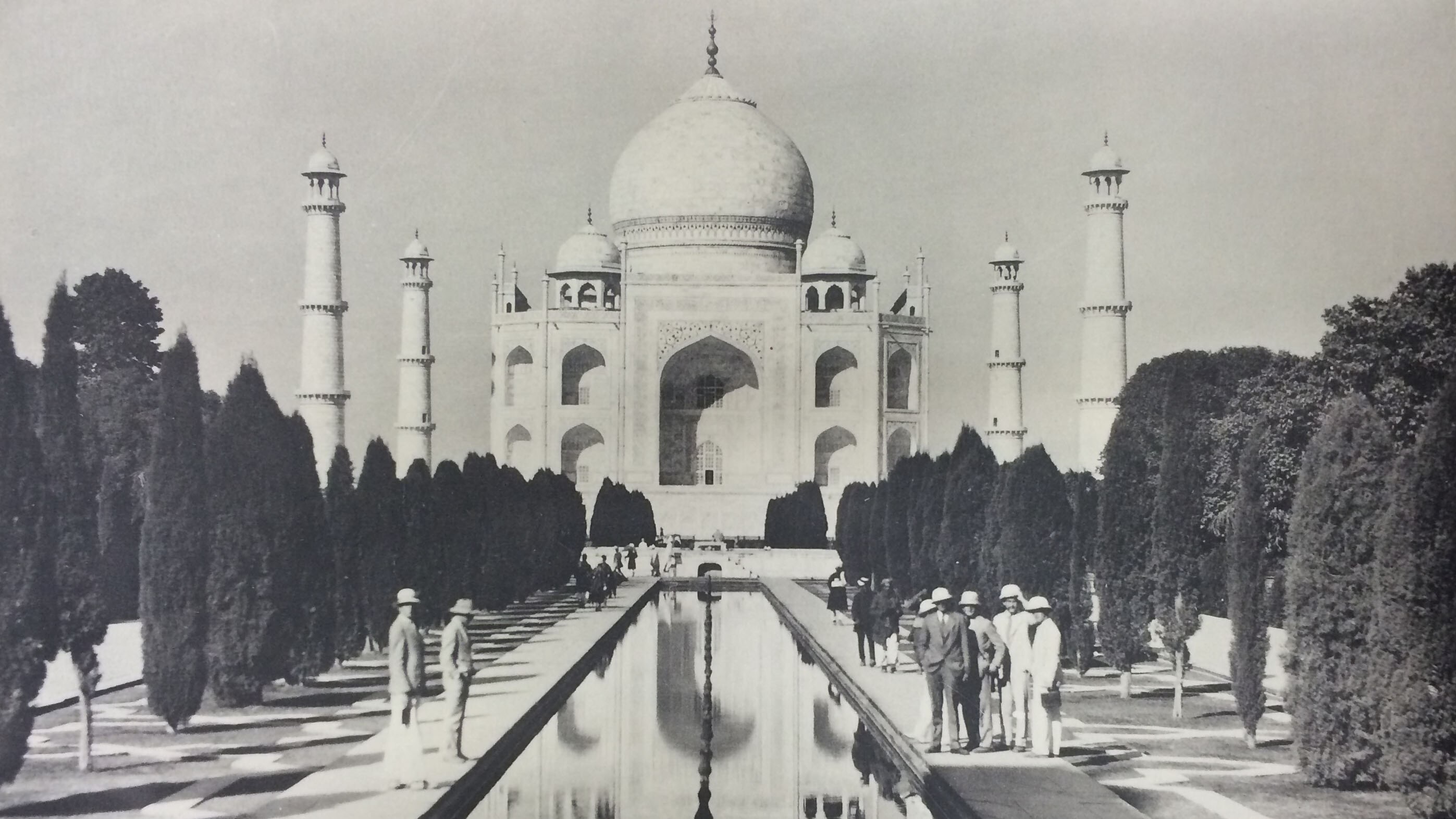 Black and white photograph of the Taj Mahal in the 1920s. Students are on either side of a pond in front of it.