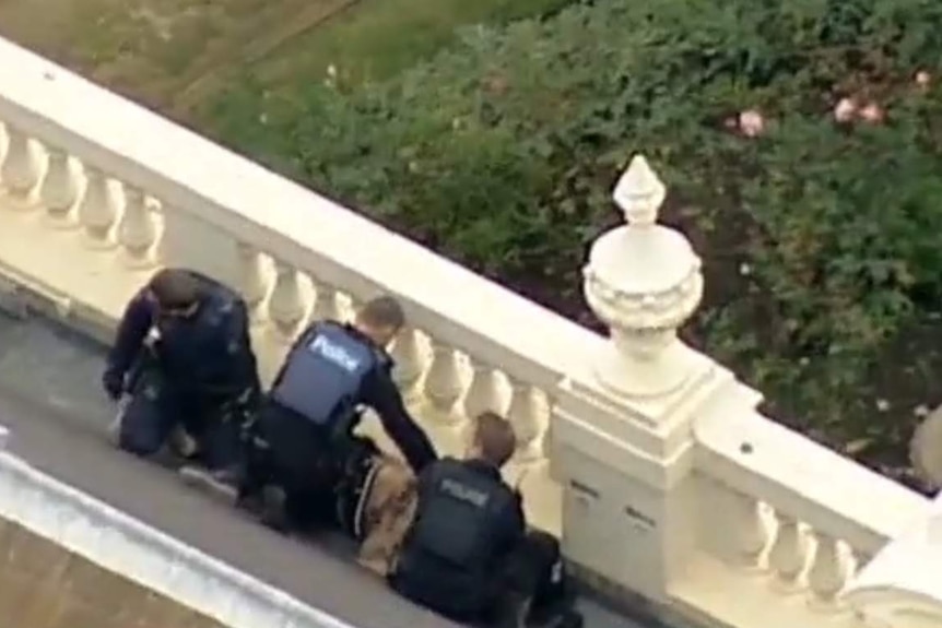 Police hold down a man on the roof of Government House in Melbourne.