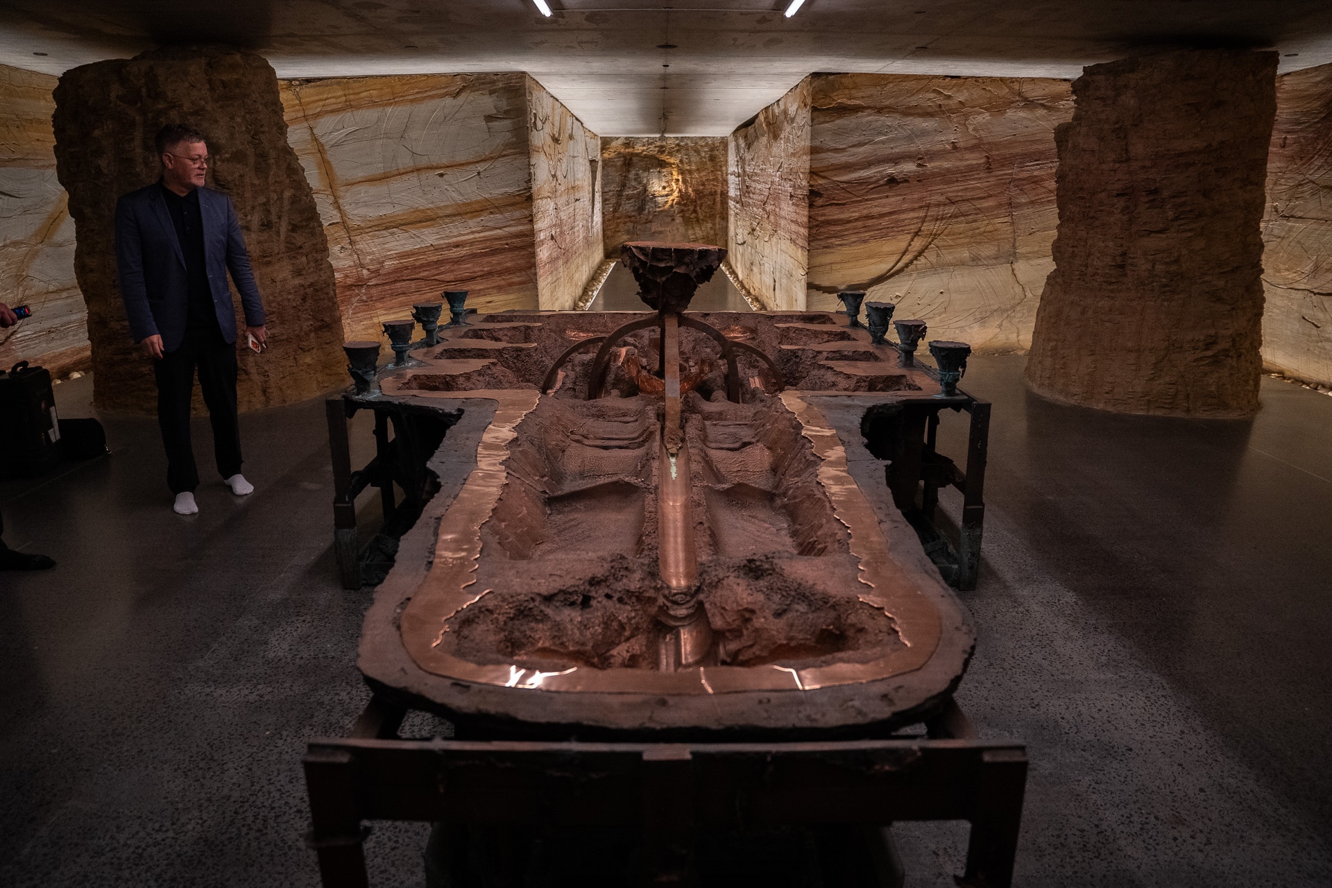 A man looks on at a massive bronze sculpture sitting in the tunnels of the Mona library.