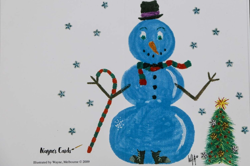 A Christmas card with a large blue snowman next to a green Christmas tree.
