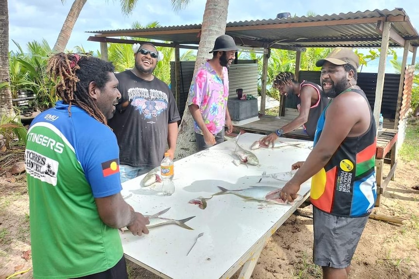 A group of men gathered around a table, gutting fish.
