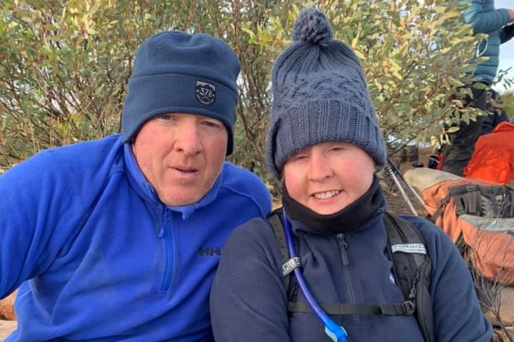 Man and woman sitting next to each other both wearing blue warm hiking clothes including beanies