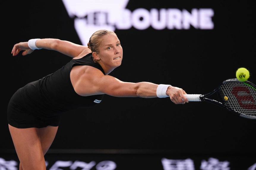 A tennis player outstretches her racquet with her right arm in