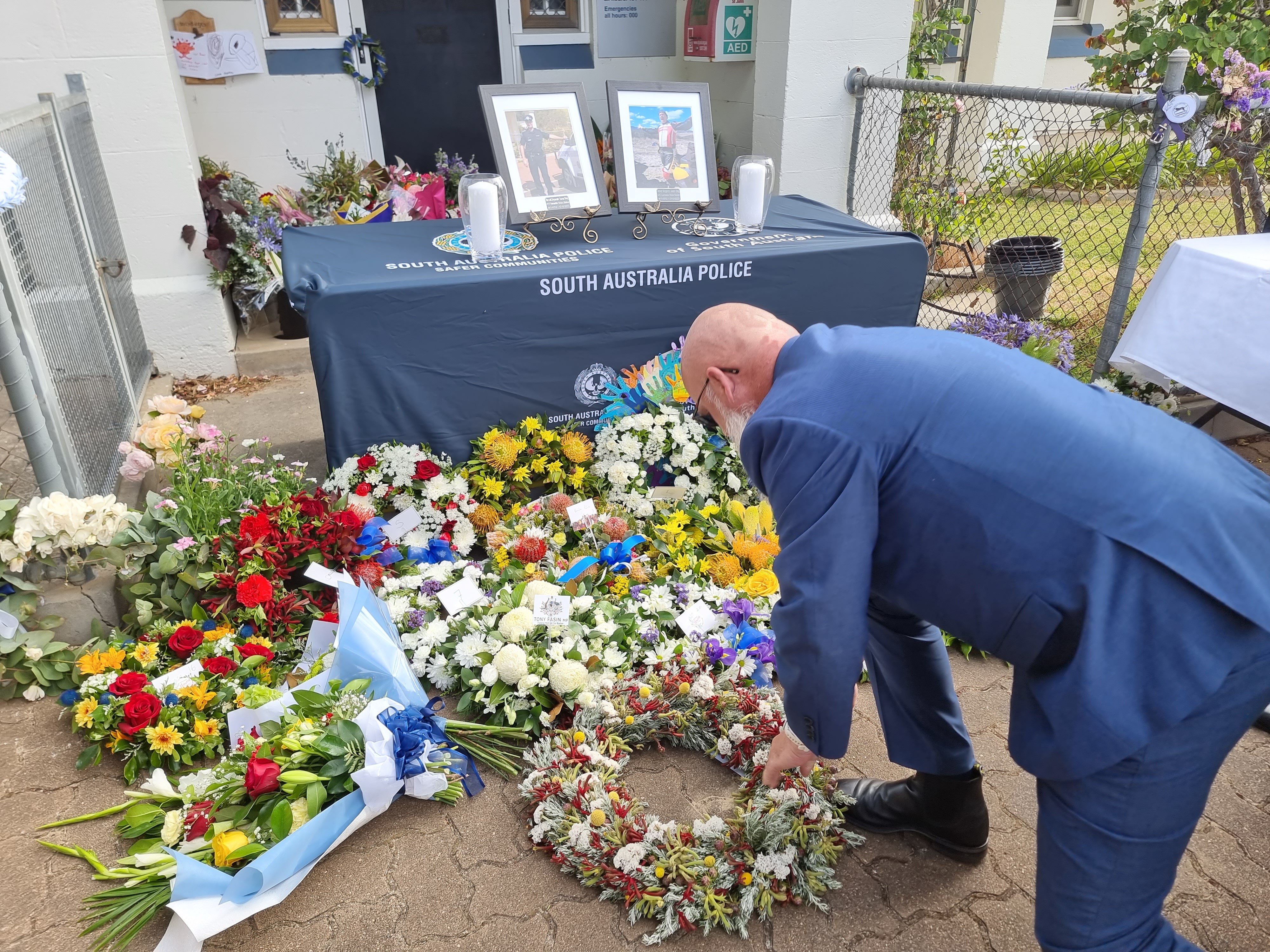 A man in a navy suit crouches down to lay a wreath at a memorial to a police officer who died on duty.