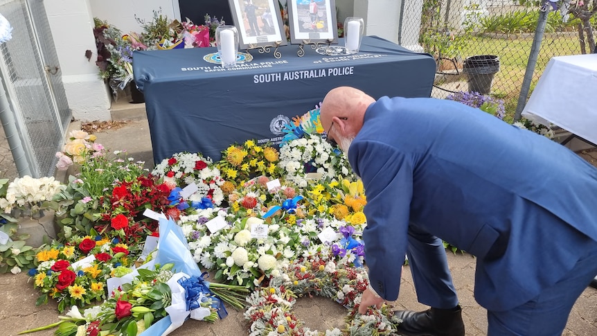 A man in a navy suit crouches down to lay a wreath at a memorial to a police officer who died on duty.