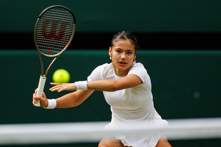 England's Emma Raducanu looks down the court with one hand off her racquet after a backhand return at Wimbledon.