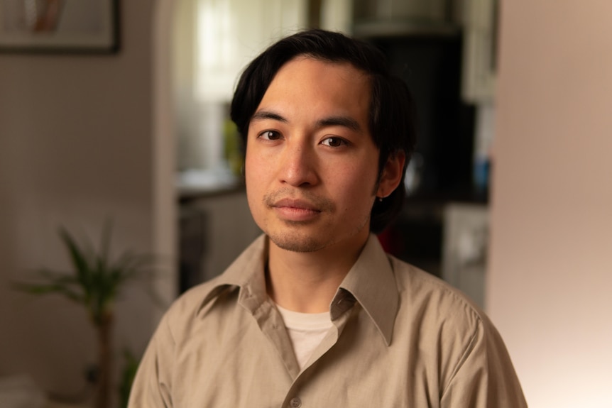 Asian man wearing beige shirt, looking at the camera. 