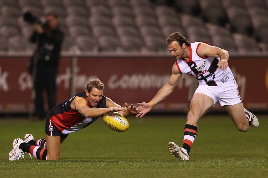 Shane Warne dives to smother the ball as Aaron Hamill contests in an AFL match 