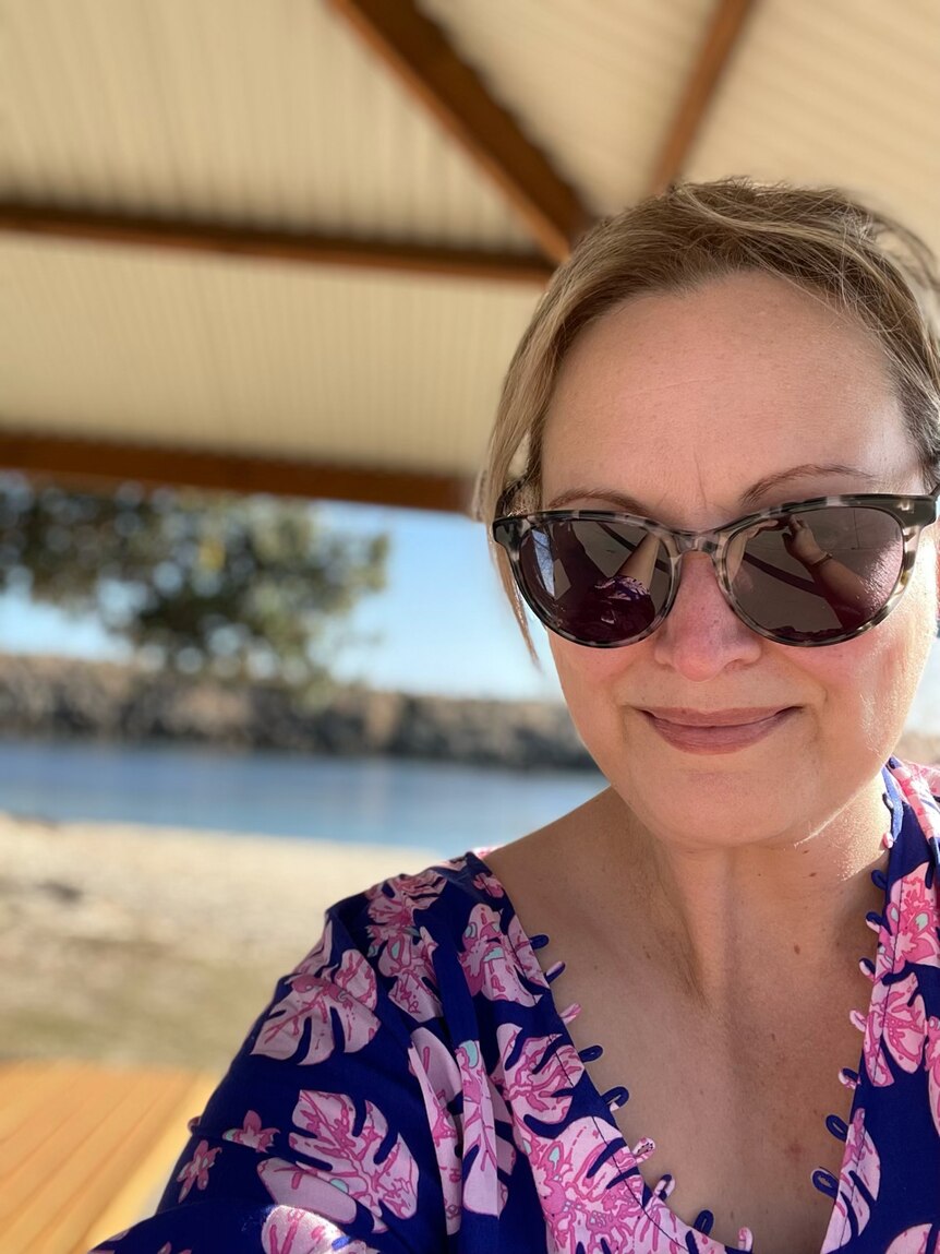 Emma Heuston, wearing a blue and pink print top and brown sunglasses, poses for a selfie