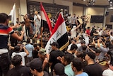 Men stand inside Iraqi parliament, holding the country's flag and taking images on phones.