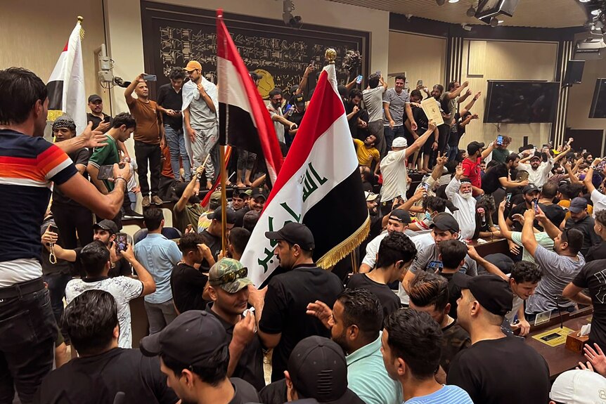 Men stand inside Iraqi parliament, holding the country's flag and taking images on phones.