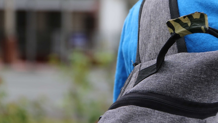 An unidentified child is seen outside a school with a backpack