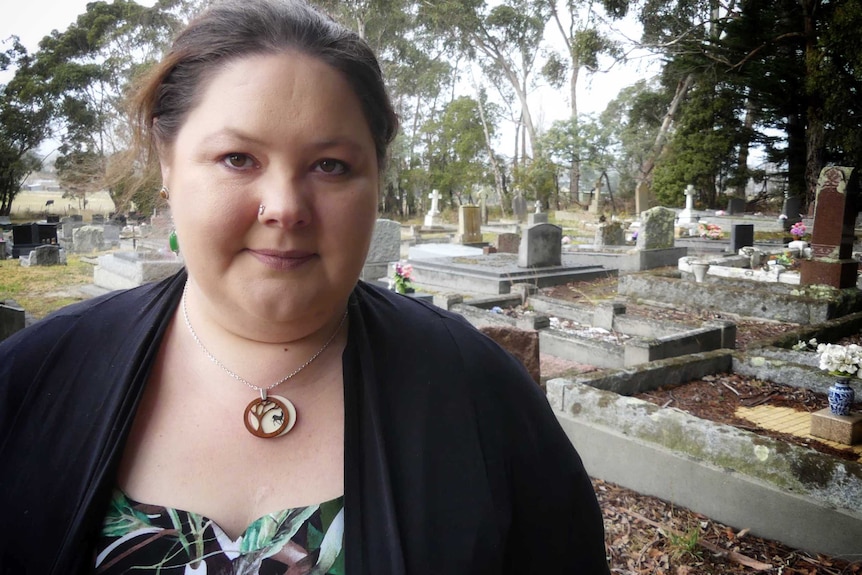 Rebecca Lyons stands at a traditional Western cemetery, with ornate gravestones marking burial site
