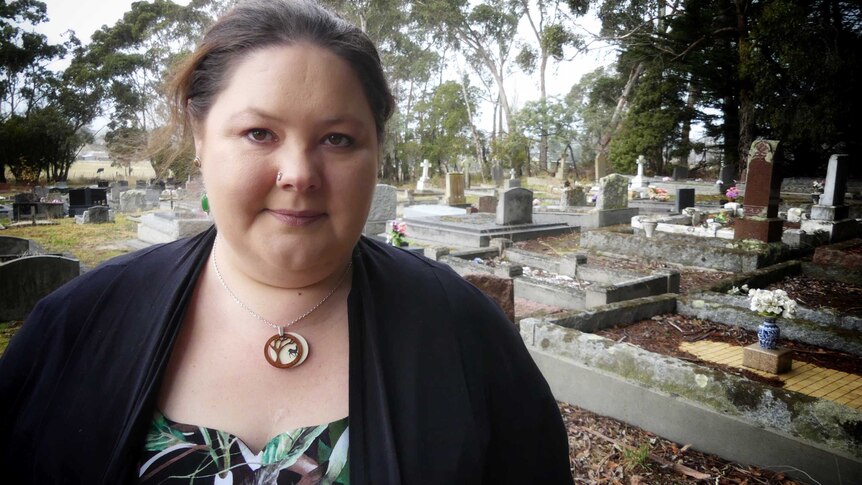 Rebecca Lyons stands at a traditional Western cemetery, with ornate gravestones marking burial site