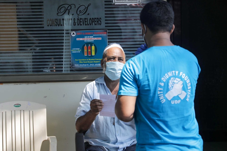 An man in a face mask talks to a man in a t-shirt