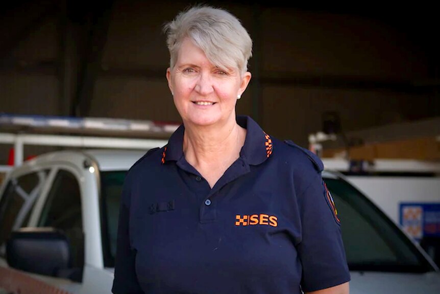 A woman wearing a black shirt with orange SES writing, smiles at the camera.