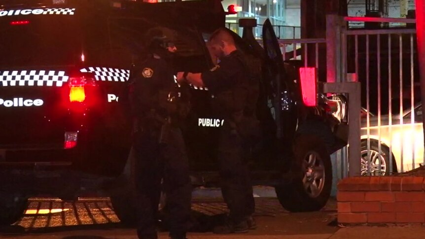 A police officer wearing riot gear faces another police officer while standing in front of a police car with flashing lights