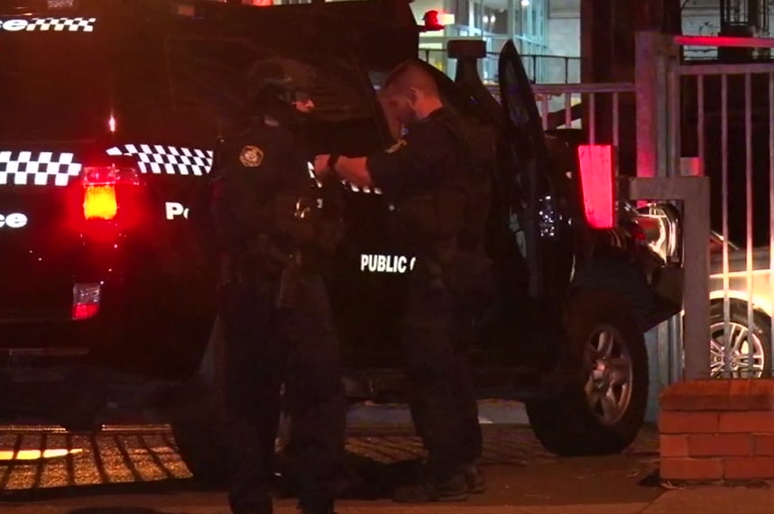 A police officer wearing riot gear faces another police officer while standing in front of a police car with flashing lights